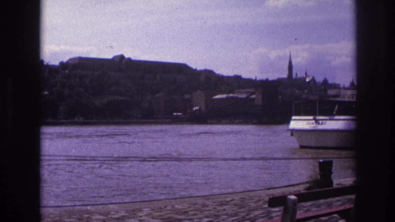 1967 France 8mm frame showing a white passenger boat on a river, seen past a dark window-like border with a cobblestone quay and distant spires.
