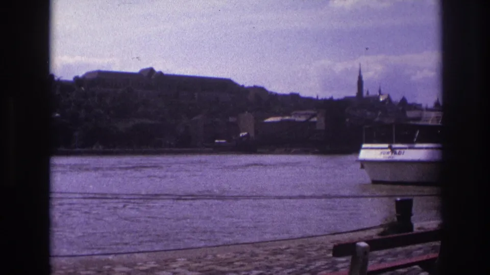 1967 France 8mm frame showing a white passenger boat on a river, seen past a dark window-like border with a cobblestone quay and distant spires.