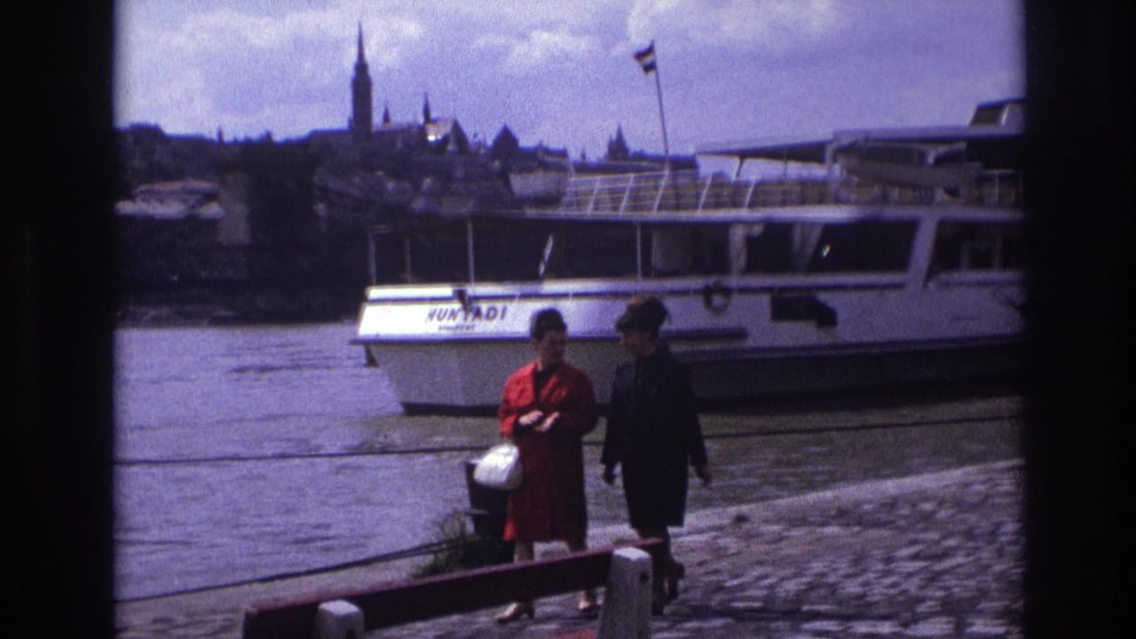 Two women continue along the waterfront with the HUNYADI boat and city skyline behind them.