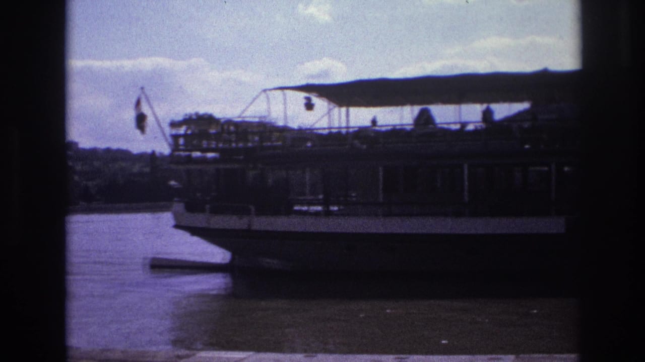 Docked passenger riverboat with canopy deck seen across calm water.
