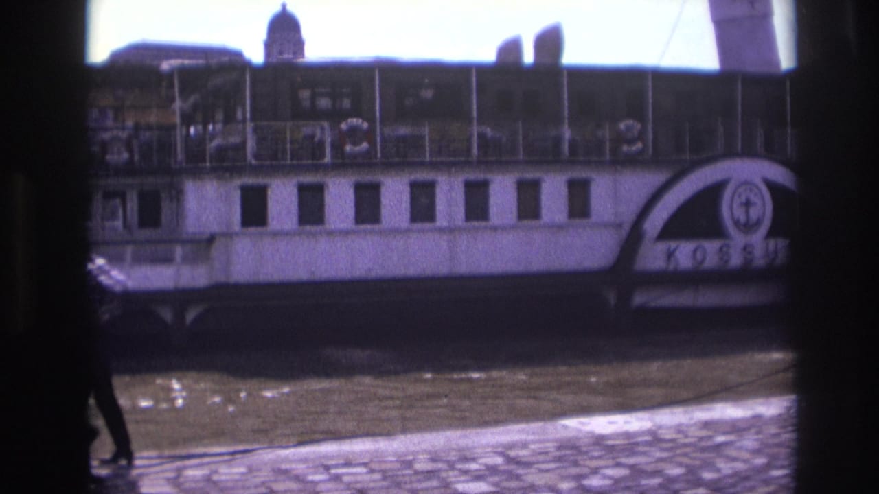 A docked white paddlewheel boat sits behind men crossing the quay.