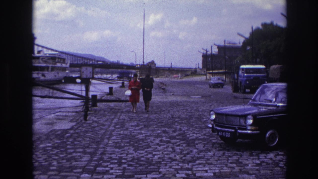 Two women continue along the cobblestones with a bridge, truck and parked car in view.