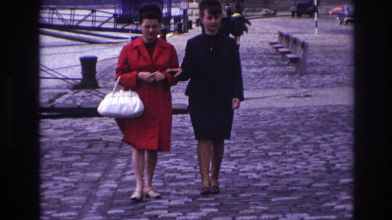 The pair faces the camera on a French riverside promenade, one in a red coat with a white handbag and one in a dark outfit.