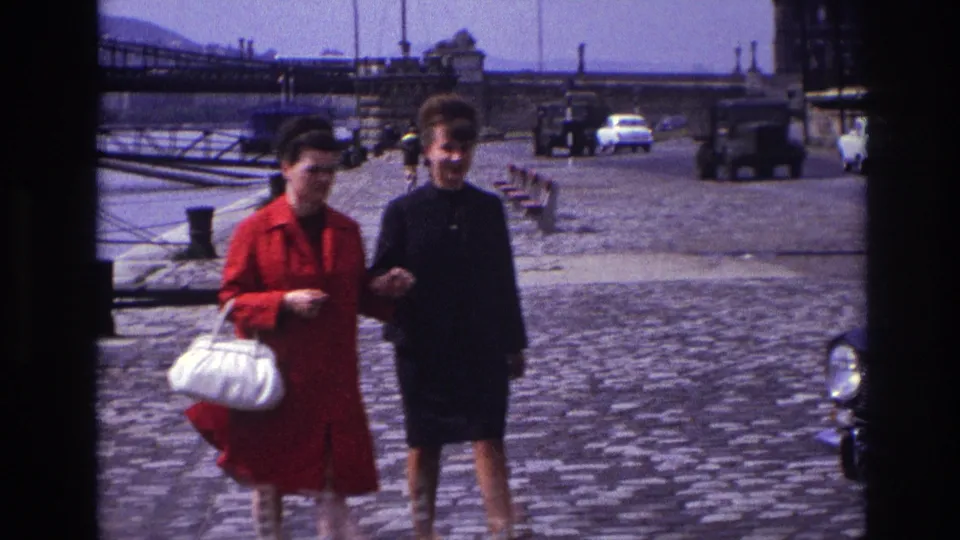 Near the end of the shot, the women come closer to the camera on a 1967 French cobblestone street, with vehicles and a bridge behind them.