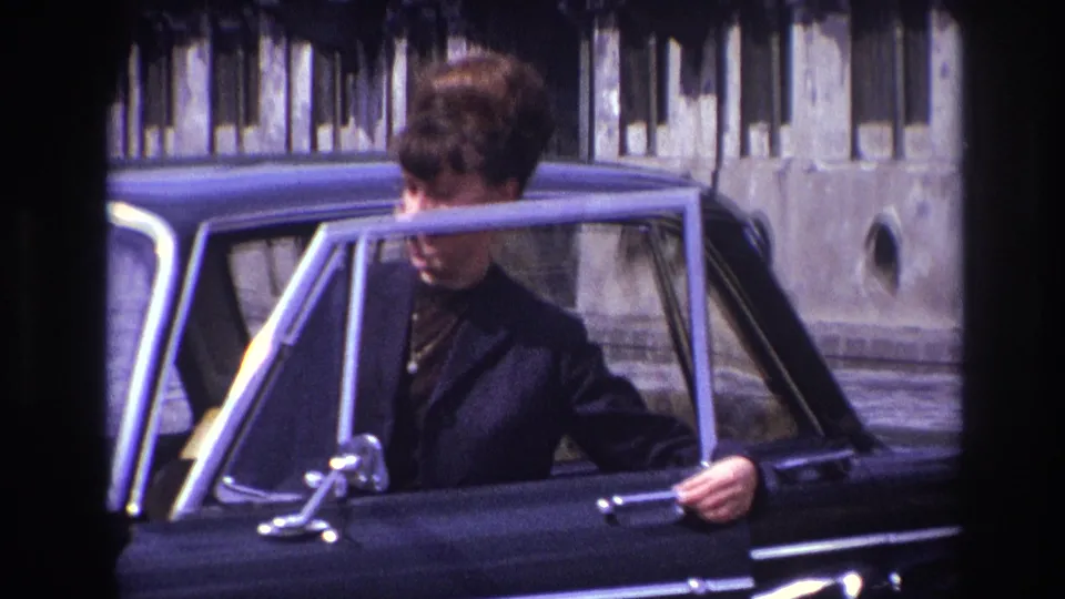 The woman is partly obscured by the open sedan door as she prepares to enter the black car in France in 1967.