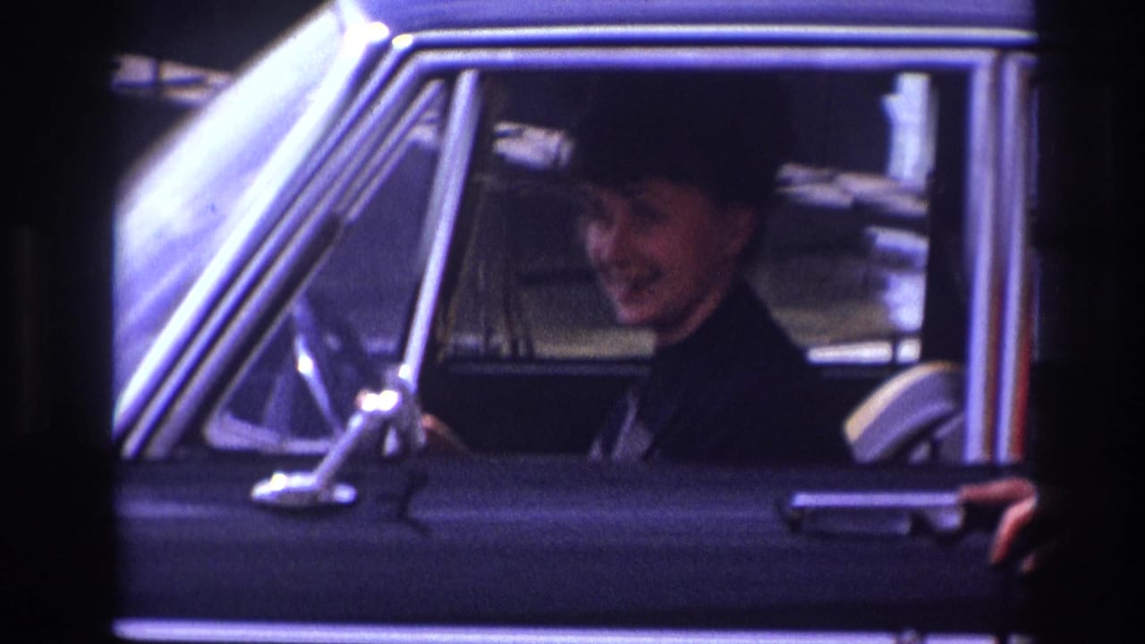 In France 1967 home-movie footage, a woman with short dark hair smiles from inside a black car.