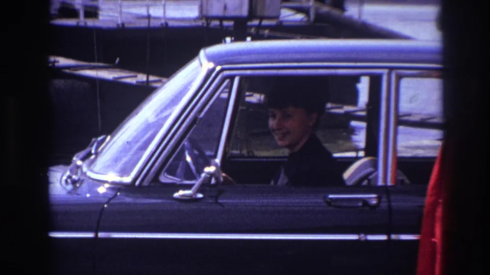 The zoom begins to reveal more of the black car and a red-coated person at the side of the frame.