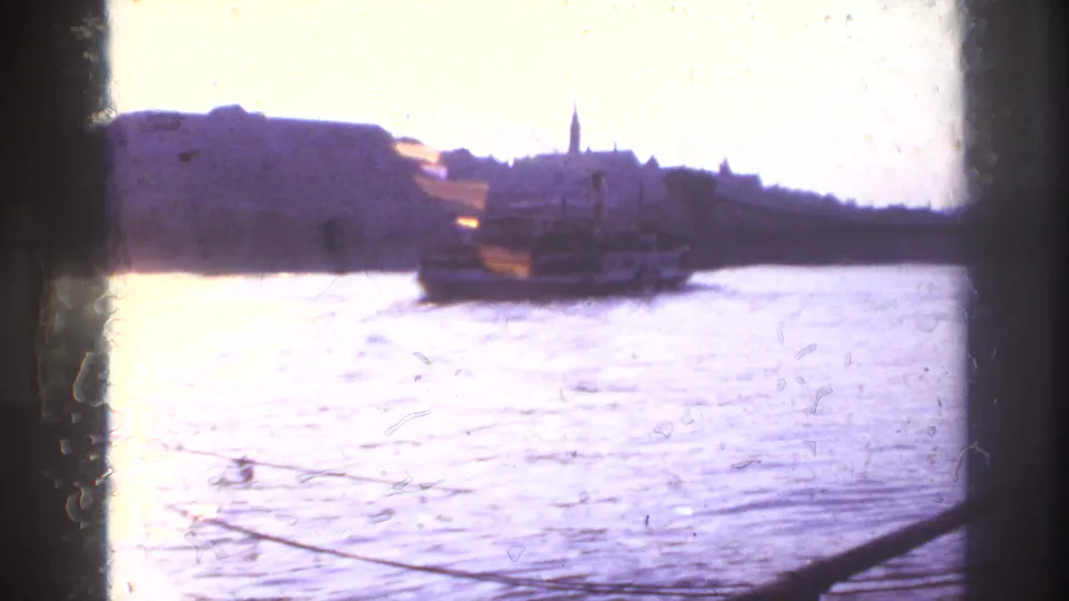 1967 France home-movie view across the river, with a boat moving near a silhouetted city shoreline and strong exposure flare.
