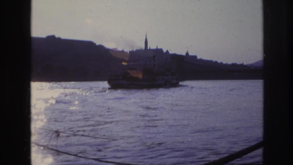 1967 France river view with a boat on the water and a dark city silhouette beyond, filmed through visible 8mm frame edges.