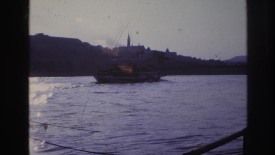 1967 France 8mm view of a ferry on a river, with a distant city skyline, church spire, and dark frame edges.