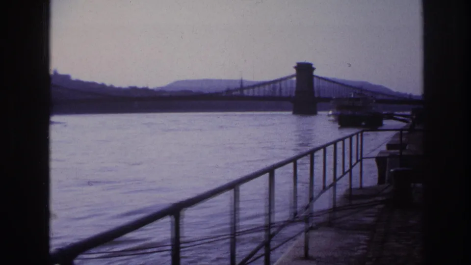 1967 France 8mm river scene framed by a railing, showing a suspension bridge and a vessel near the right edge.