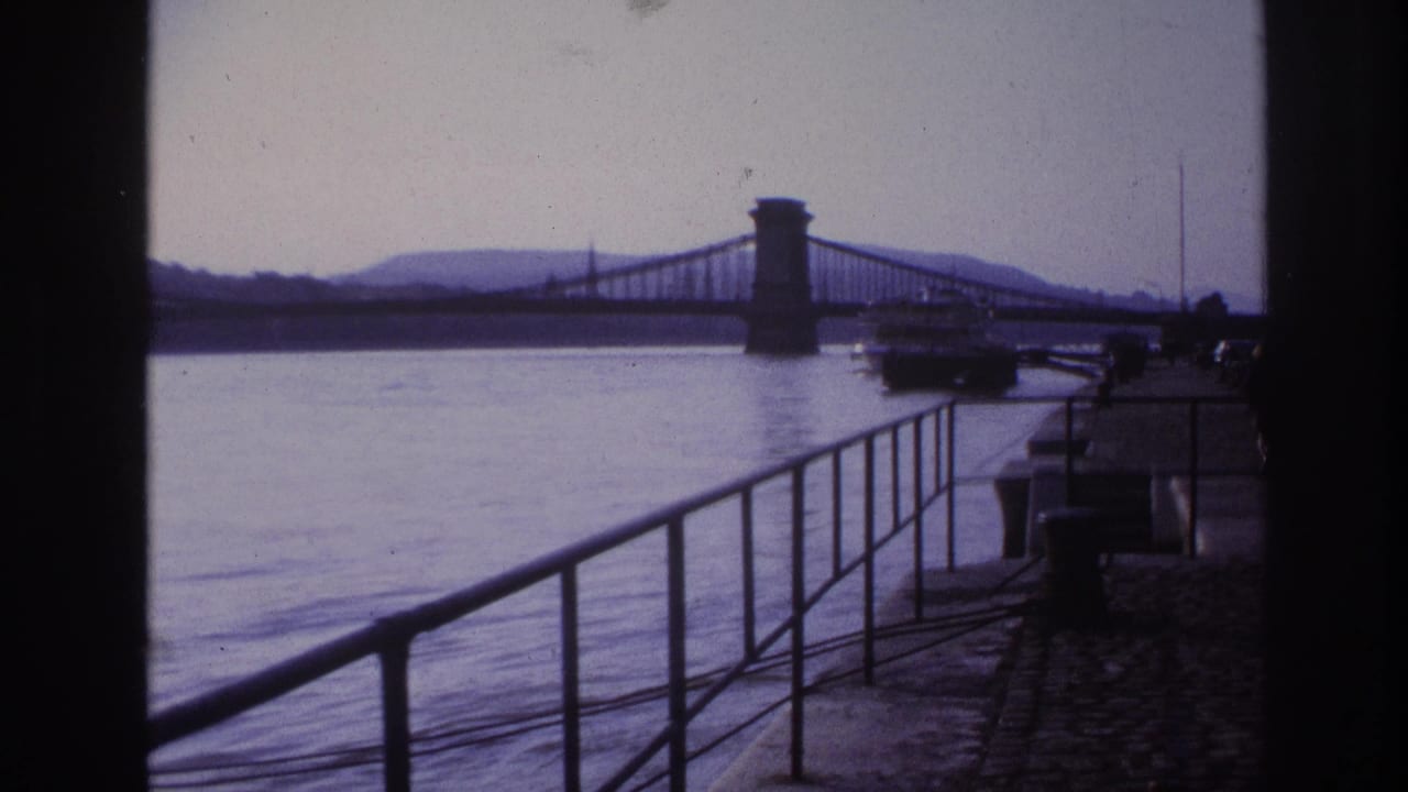 1967 8mm travel frame showing a waterfront railing, broad river or harbor, distant suspension bridge, and shadowed bridge approach in France metadata.
