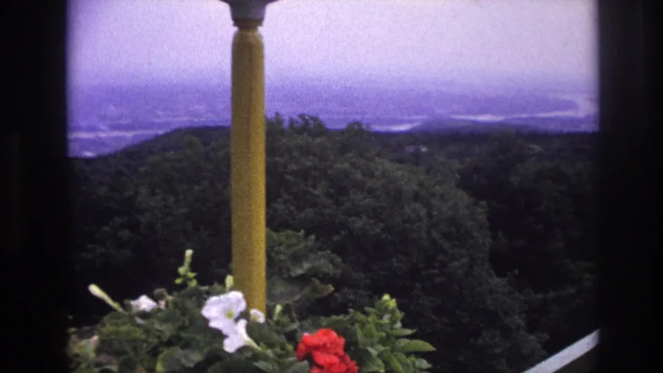 1967 France 8mm frame showing a yellow balcony column, flower boxes, trees, and hazy distant water.