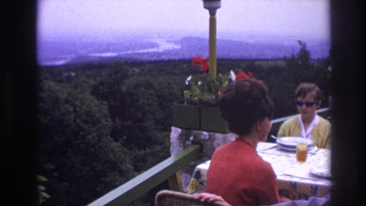 Woman sits with her back partly to camera while a child faces her across a terrace table.