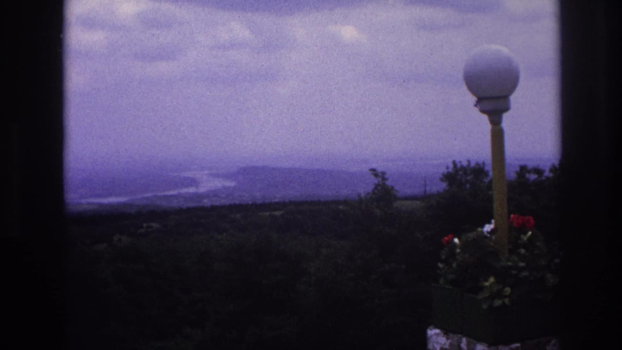 1967 France home-movie view of a hazy river landscape, framed by dark edges with a white globe lamp and red flowers in the foreground.