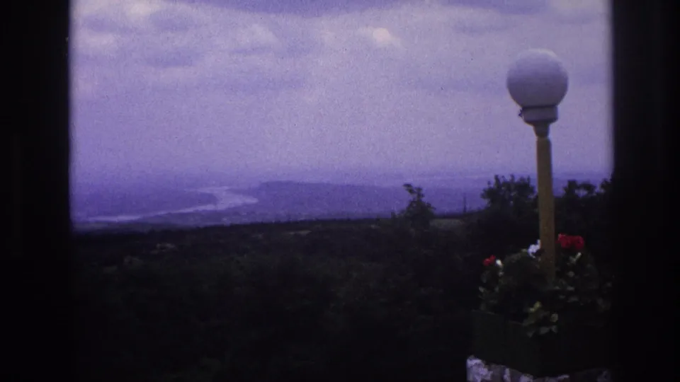 1967 France home-movie view of a hazy river landscape, framed by dark edges with a white globe lamp and red flowers in the foreground.