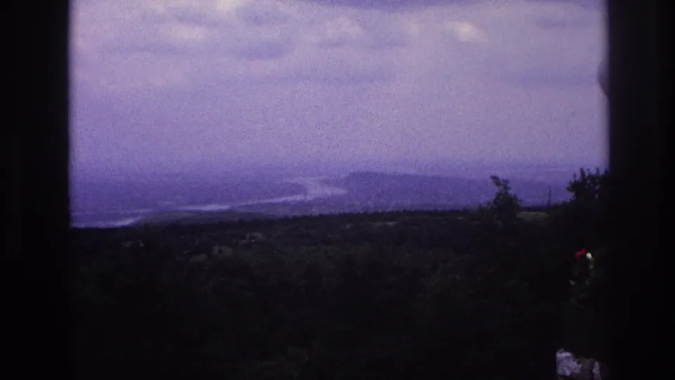 Soft 8mm view of a cloudy French landscape with distant water, wooded hills, and dark window or balcony edges.