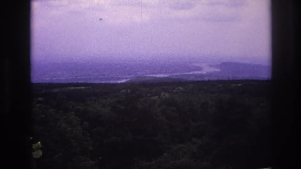 Purple-shifted 8mm frame of a French countryside view with a distant river bend, hills, and dark window edges.
