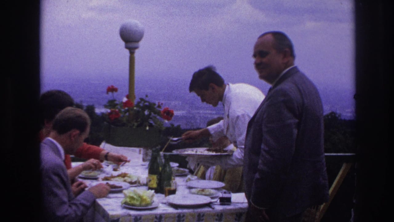 A French terrace lunch scene from 1967 shows men in suits eating while a waiter serves and another suited man stands at the table edge.