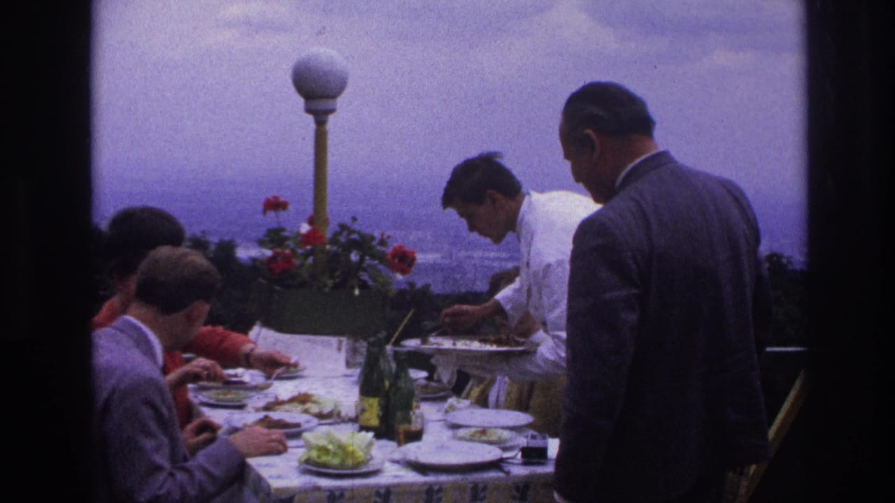 A waiter serves a rooftop dining table with adults seated around it.