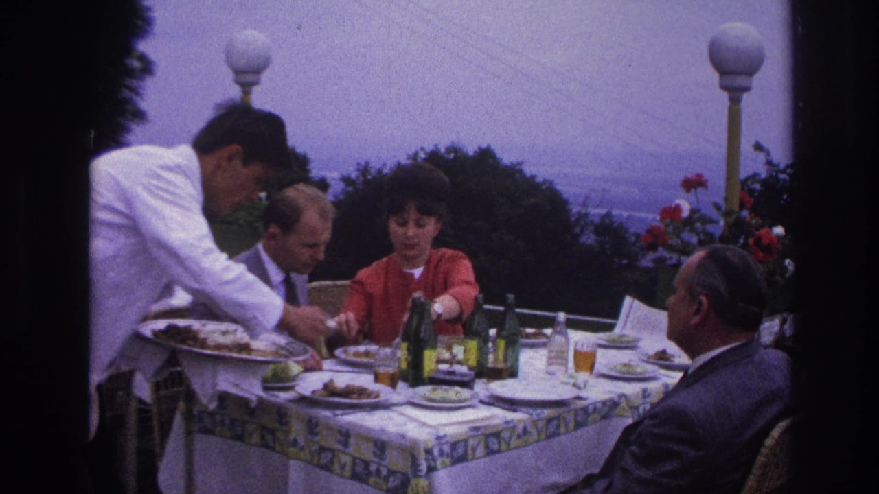 Waiter leaning over a terrace table while adults continue lunch.