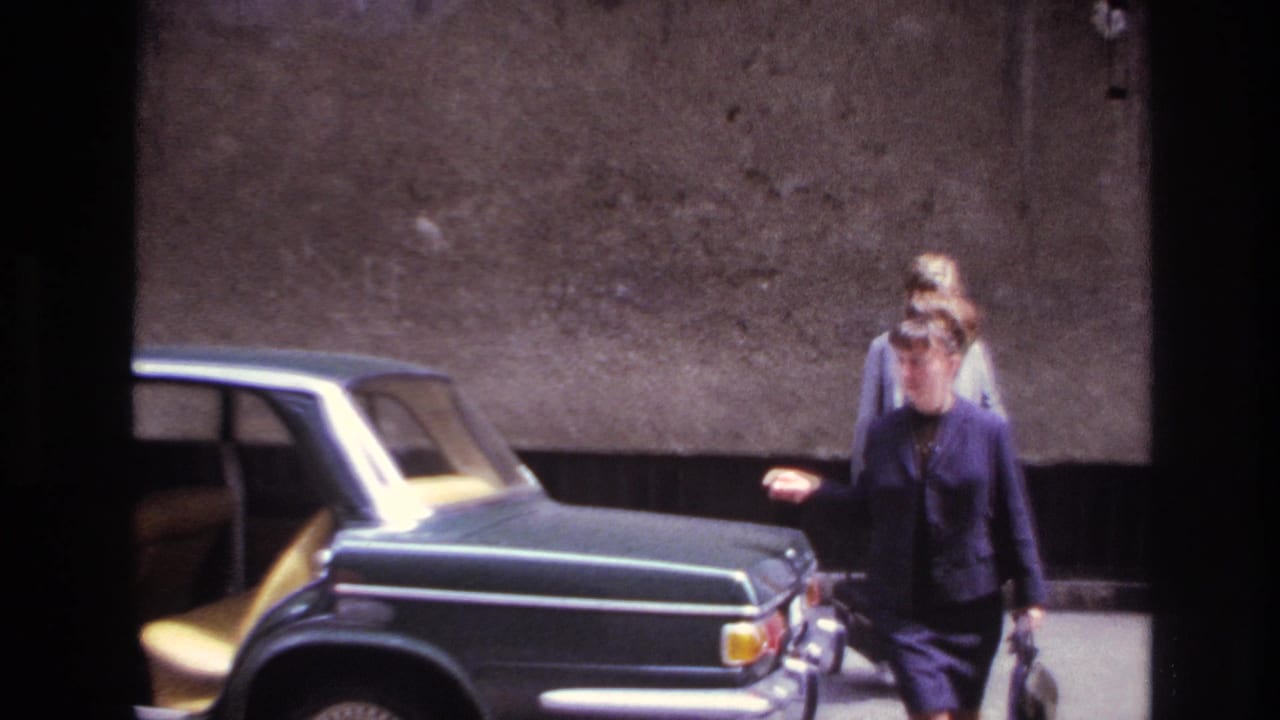A woman in a dark suit walks away from an open sedan door.
