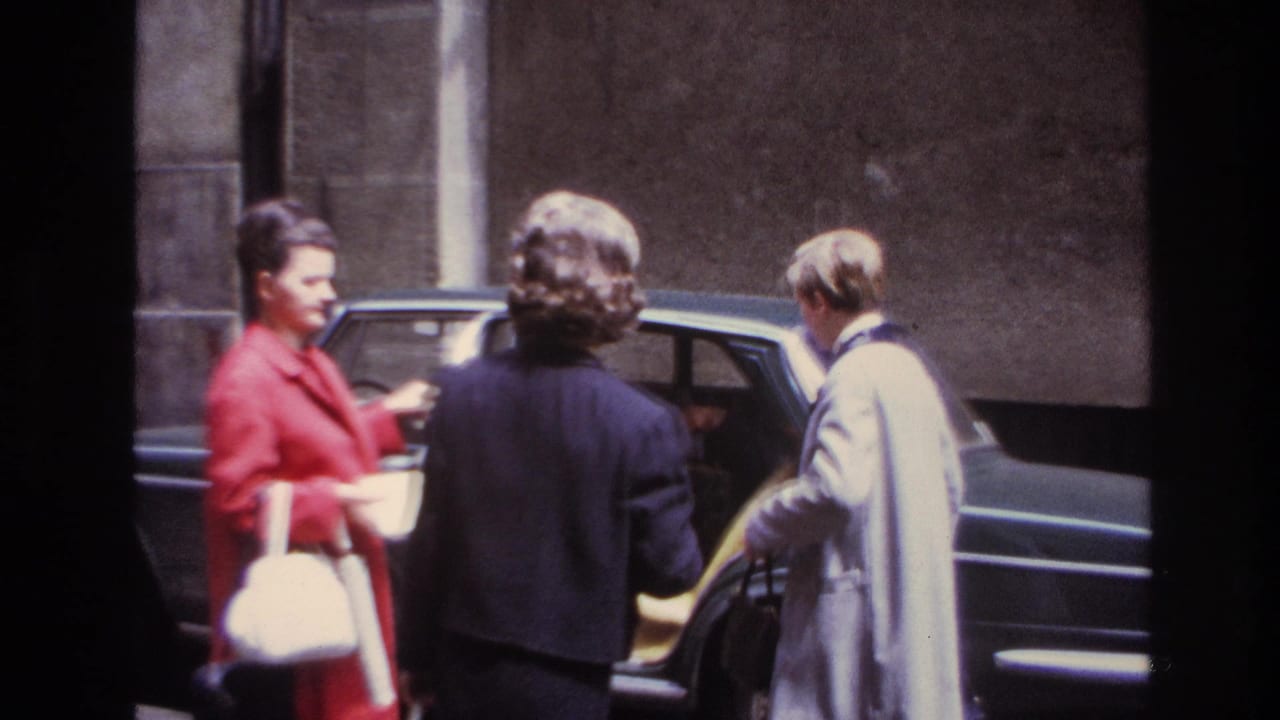 Three adults gather at the open rear door of a dark sedan.