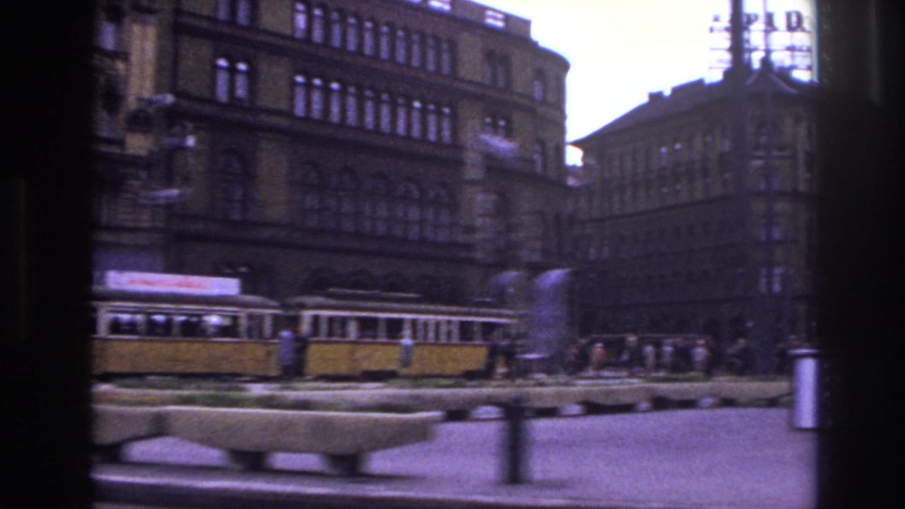 1967 France street view with a yellow tram, pedestrians, planters, poles, and older masonry buildings seen from a moving vehicle.