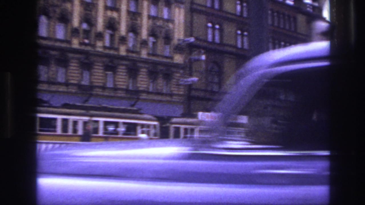 Blurred vehicle passes in front of trams and ornate street buildings.