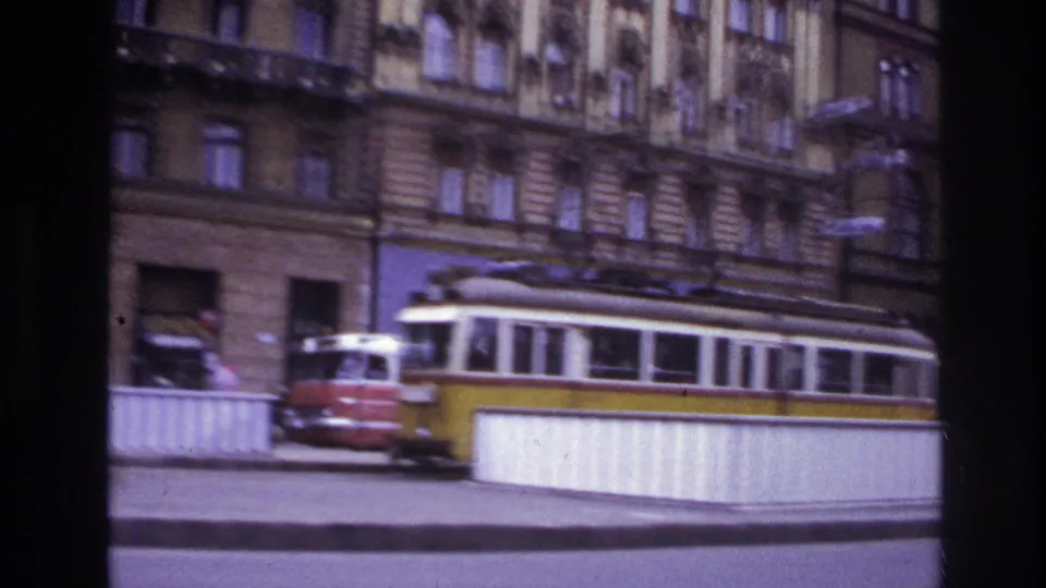 1967 France city street with a red and yellow tram, railings, building entrances, shopfronts, and soft handheld 8mm blur.