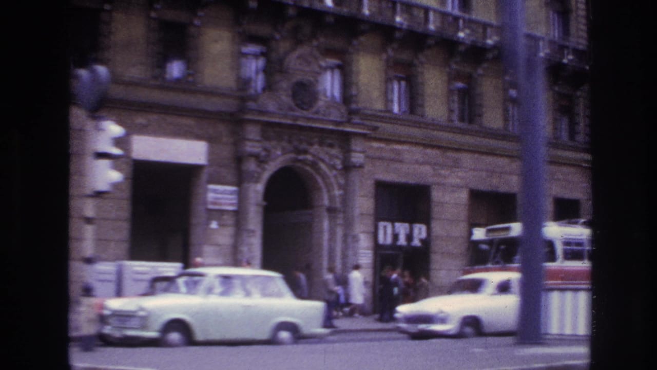1967 France street view with compact cars, pedestrians near shopfronts, building facades, and a red and white trolley or street fixture.