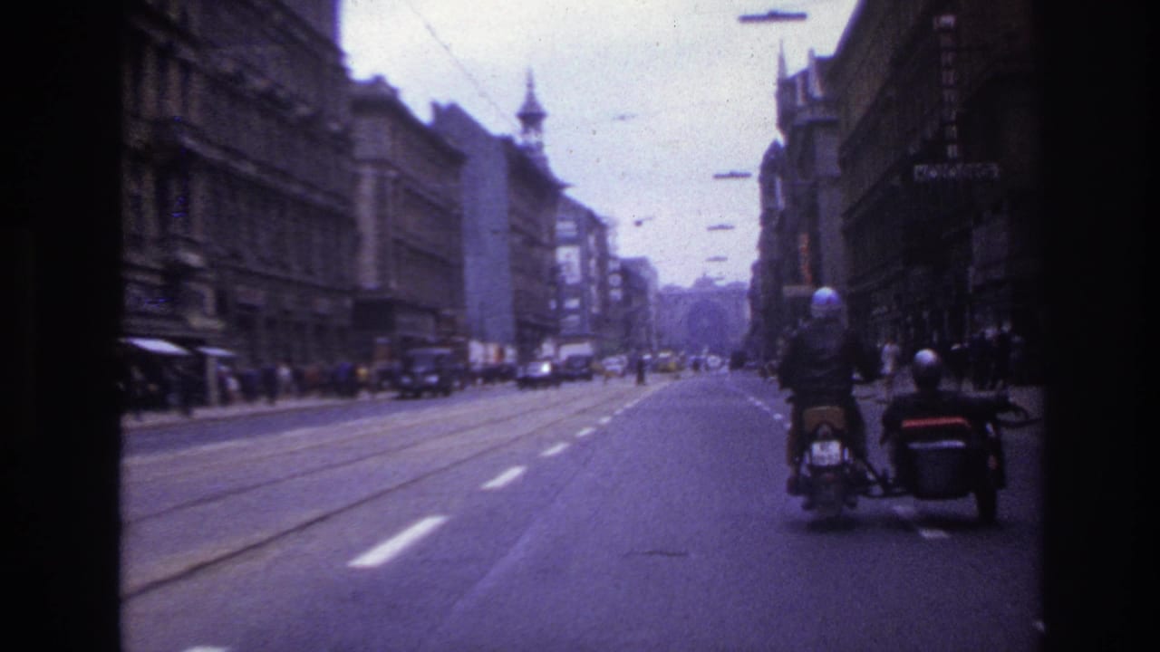 1967 France street view from a moving vehicle, with tram tracks, pedestrians, older buildings, cars, and a motorcycle with sidecar in front.
