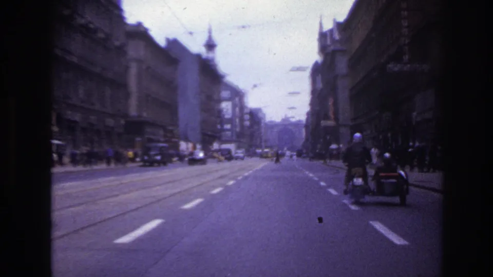 Forward-facing 1967 France street footage shows a motorcycle with sidecar, tram rails, cars, pedestrians, and dense urban buildings.