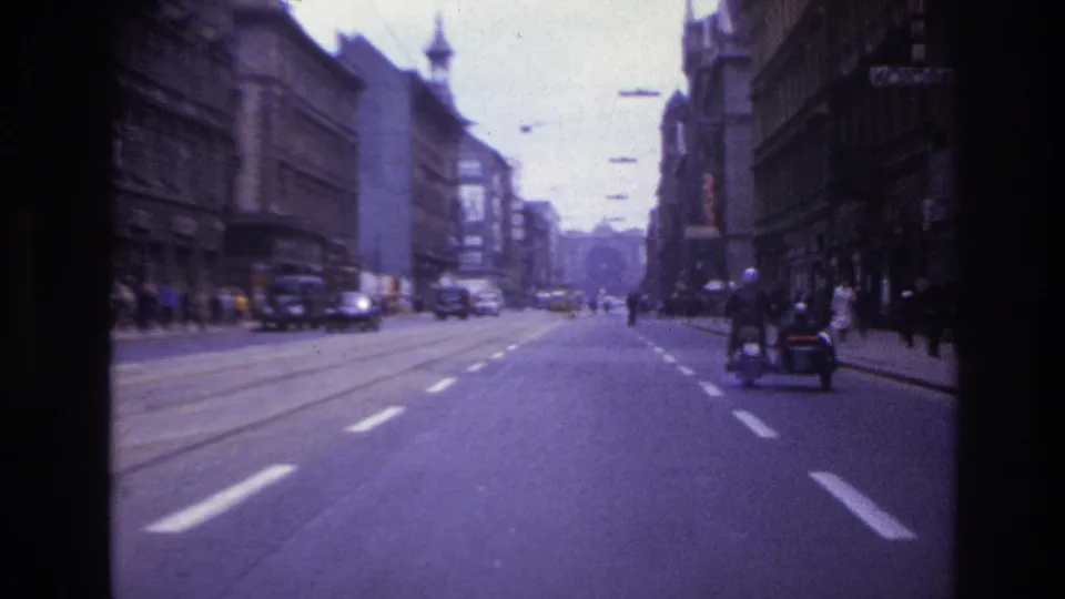 A 1967 France driving view shows tram tracks, mid-century cars, pedestrians, tall buildings, and a sidecar motorcycle near the right curb.