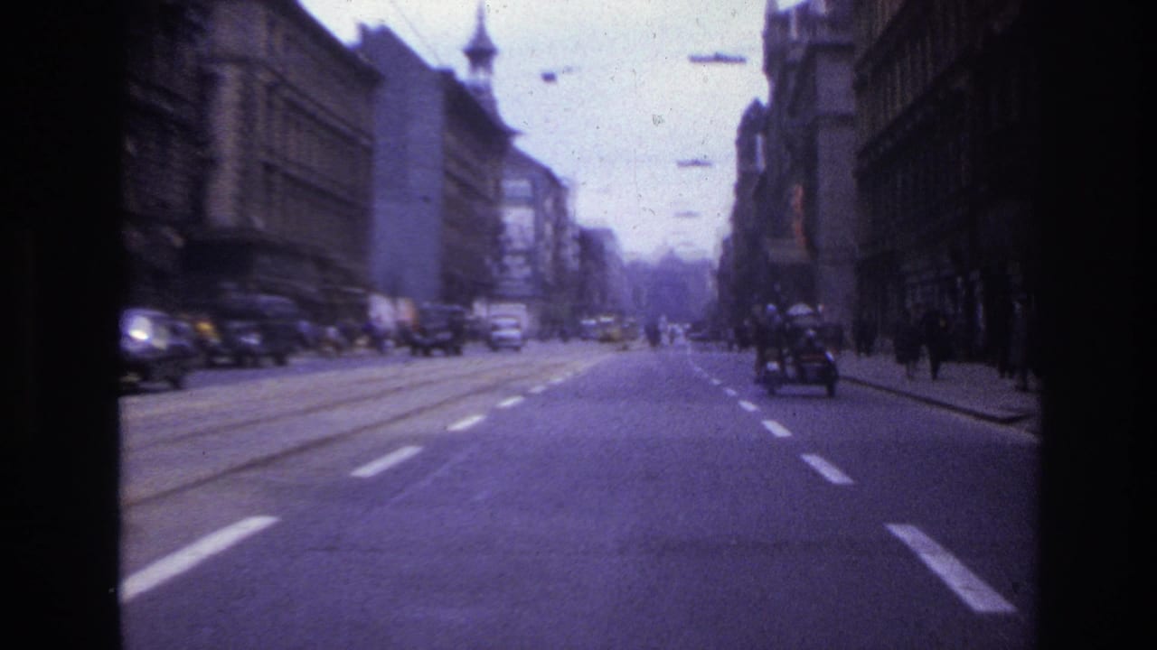 1967 France home-movie view down a broad city street with classic cars, pedestrians, road markings, and older buildings.