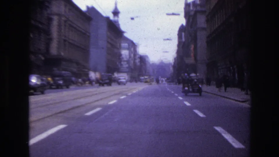 1967 France home-movie view down a broad city street with classic cars, pedestrians, road markings, and older buildings.