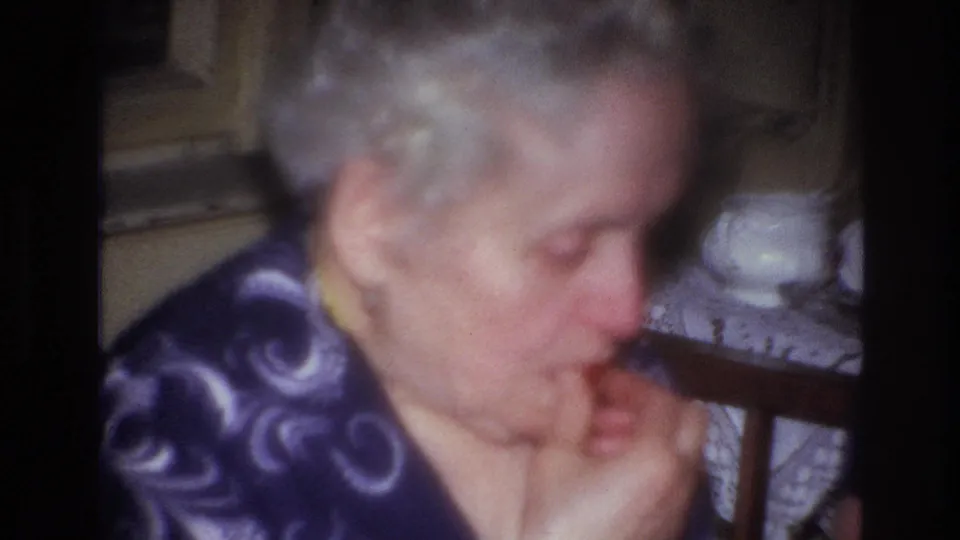 A soft-focus 1967 France home-movie close-up shows an older woman eating in a dim private room.