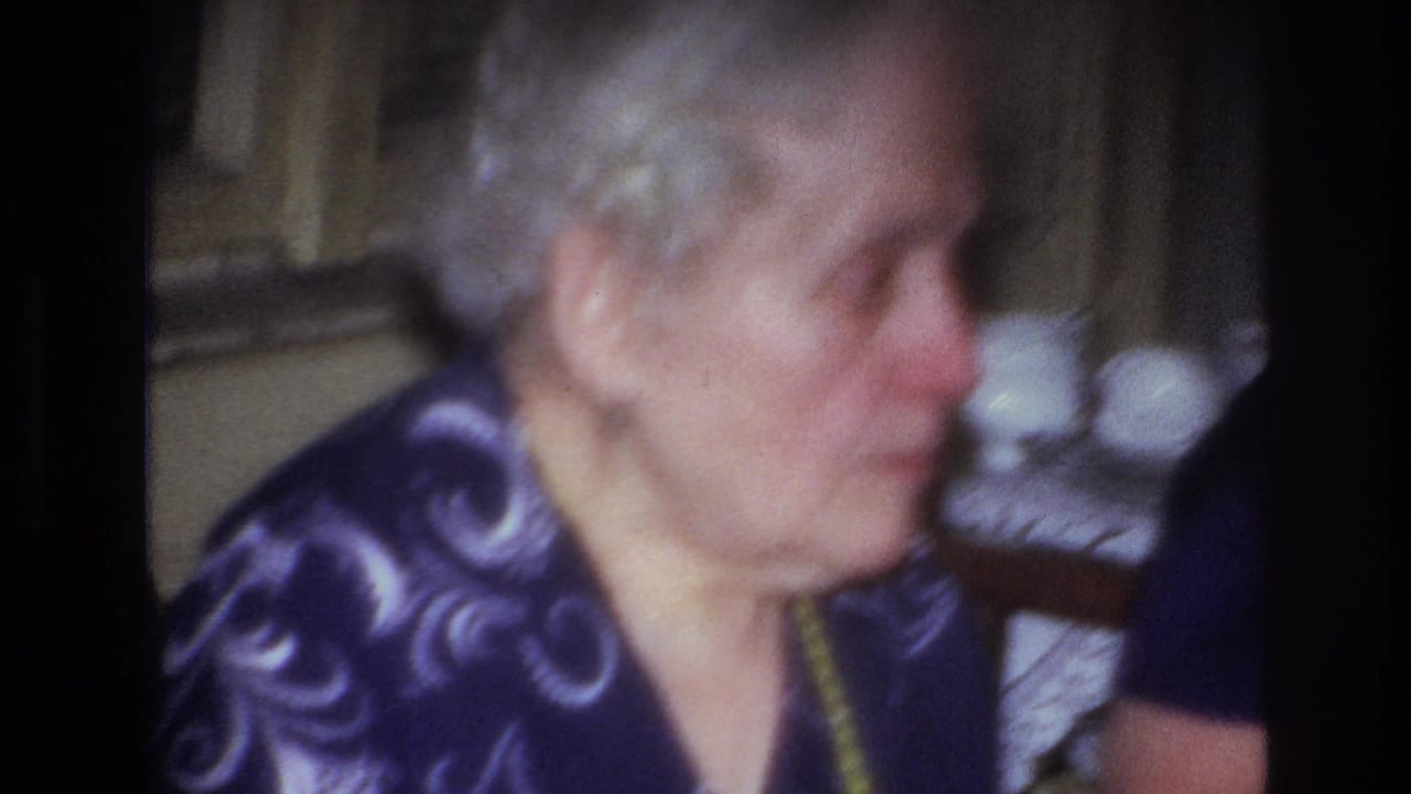Close view of an elderly woman in profile seated inside a home.