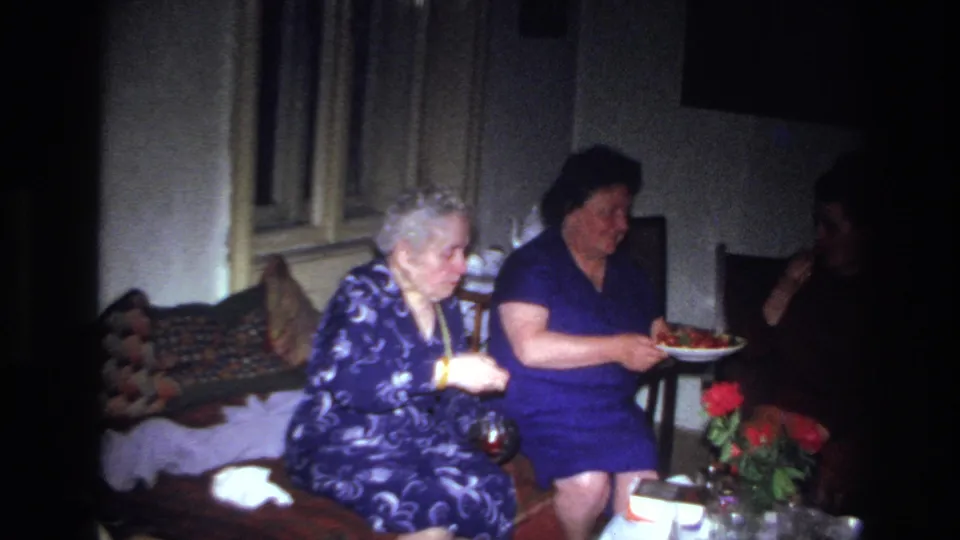 A 1967 France home interior shows two women seated near fruit, flowers, and a small table in soft 8mm light.
