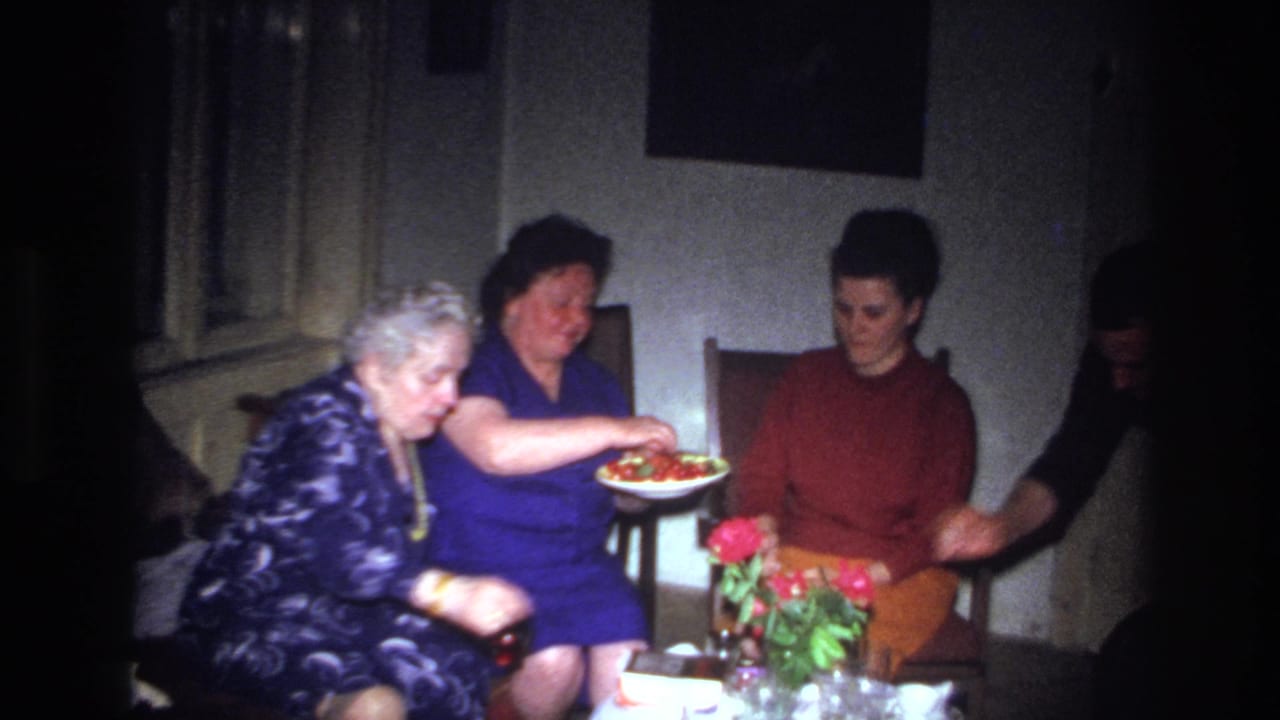 Three women seated near flowers while another person is partly visible at the edge.