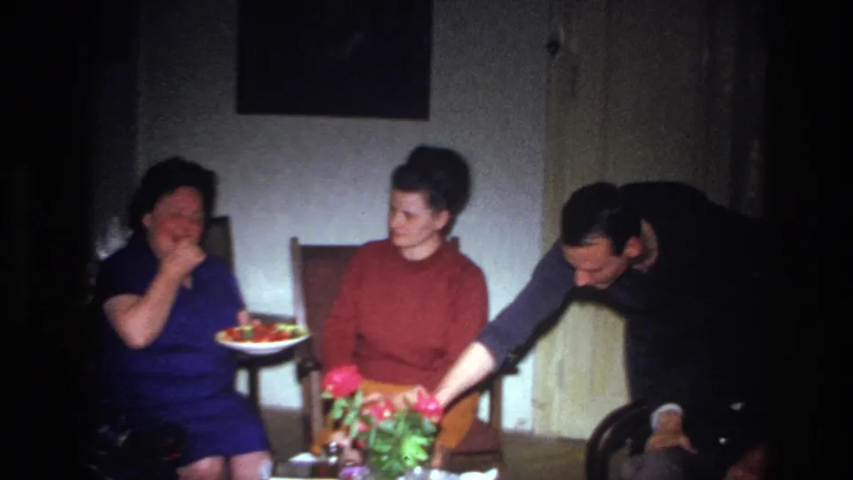 At the end of the 1967 French 8mm dinner clip, two seated women face each other while a man leans toward the small table with flowers in the dim living room.
