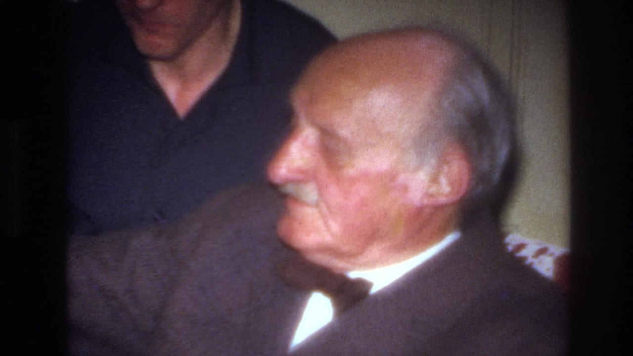 Close view of the elderly man seated sideways with the younger man partly visible behind him.