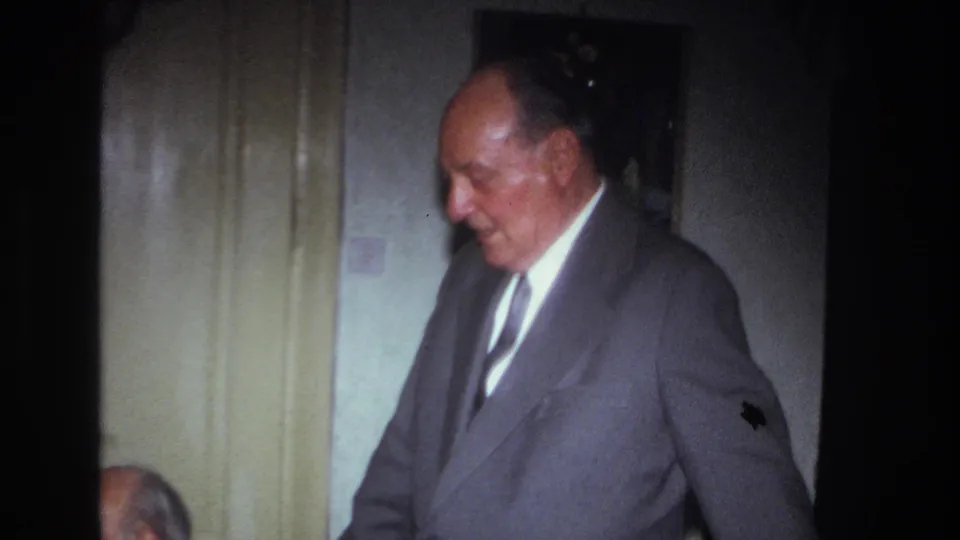1967 France home-movie close view of a gray-suited adult man standing indoors near pale doors during a gathering.