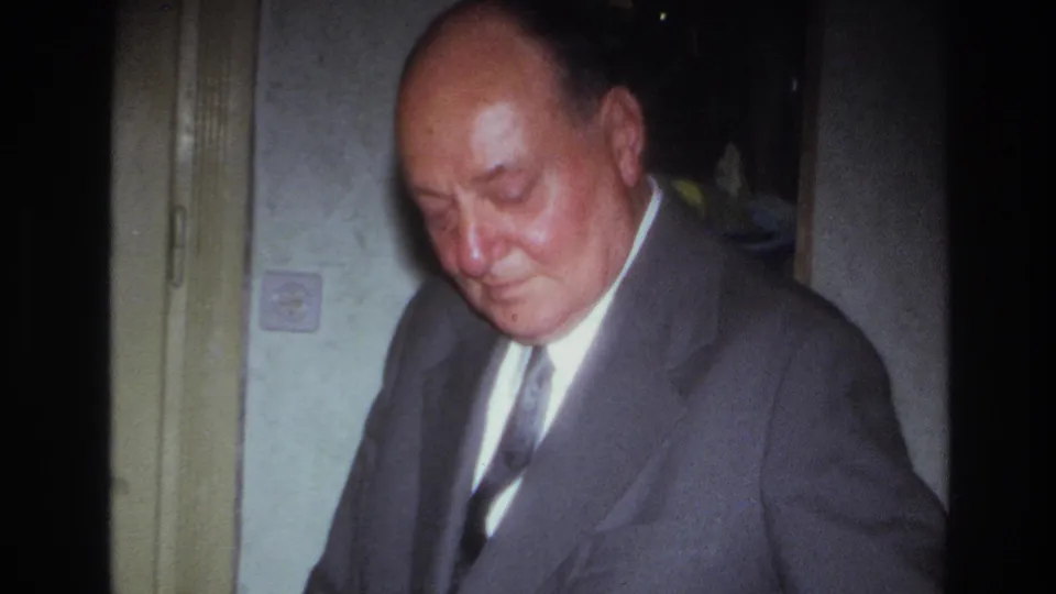 1967 France home-movie frame showing a close view of a suited adult man in a private interior during a meal or gathering.