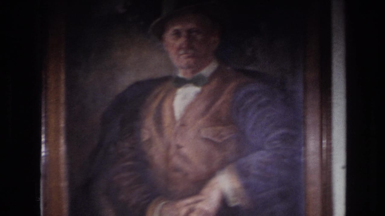 1967 France 8mm frame showing a close view of a framed painted portrait of an older man in a bowler hat, bow tie, and vest.