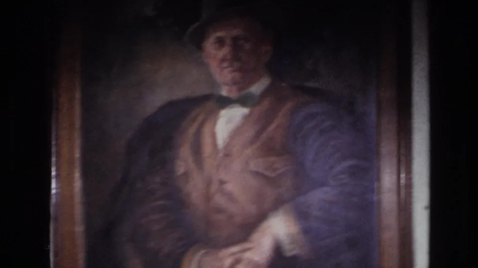 1967 France 8mm frame showing a close view of a framed painted portrait of an older man in a bowler hat, bow tie, and vest.