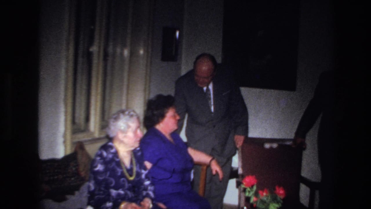Two seated women look toward a standing man while another figure enters from the right.