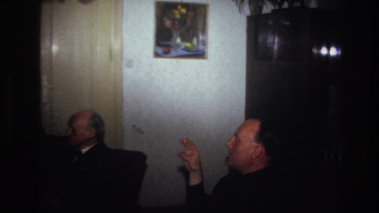 Older men sit in profile in a dark room with a wooden cabinet, wall painting, and glassware behind them.
