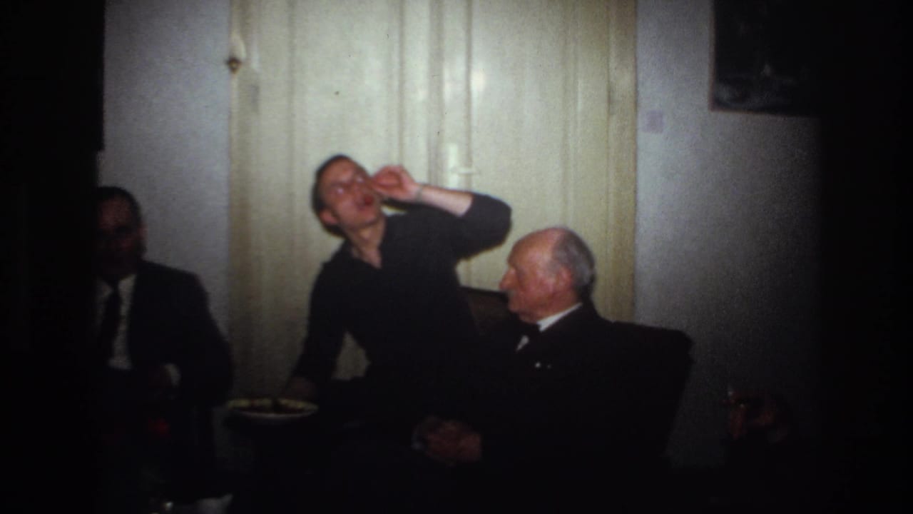 A seated man lifts his hand toward his mouth while an older man watches.