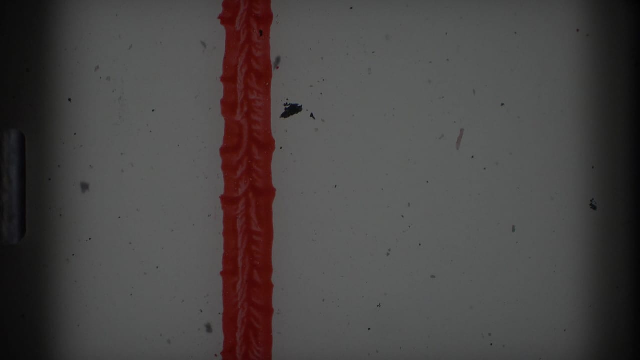 8mm film edge or leader area with a vertical red stripe, dark vignette, dust, and surface marks from the scan.